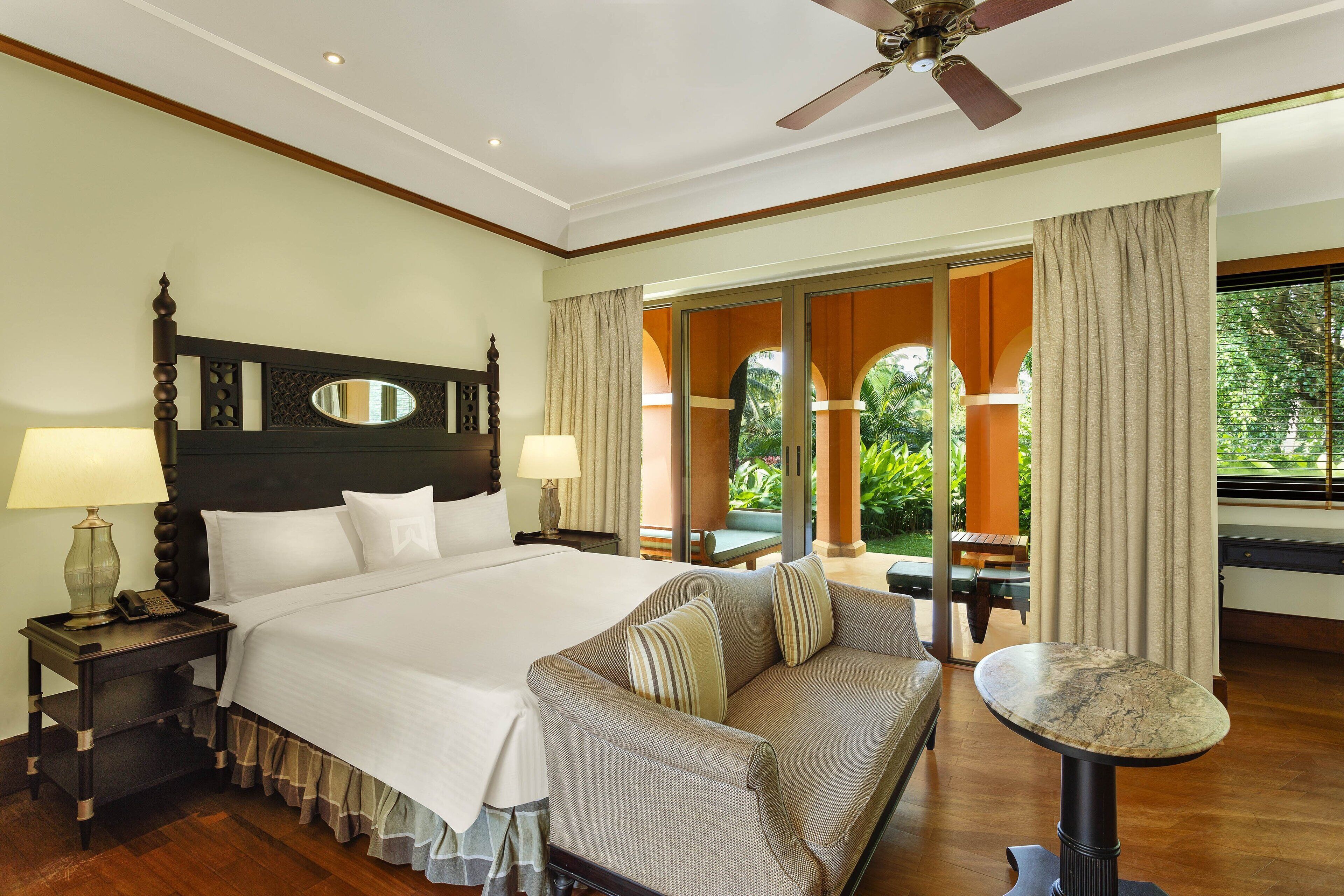 A hotel room with a large bed, a sofa, a small table, and a ceiling fan.