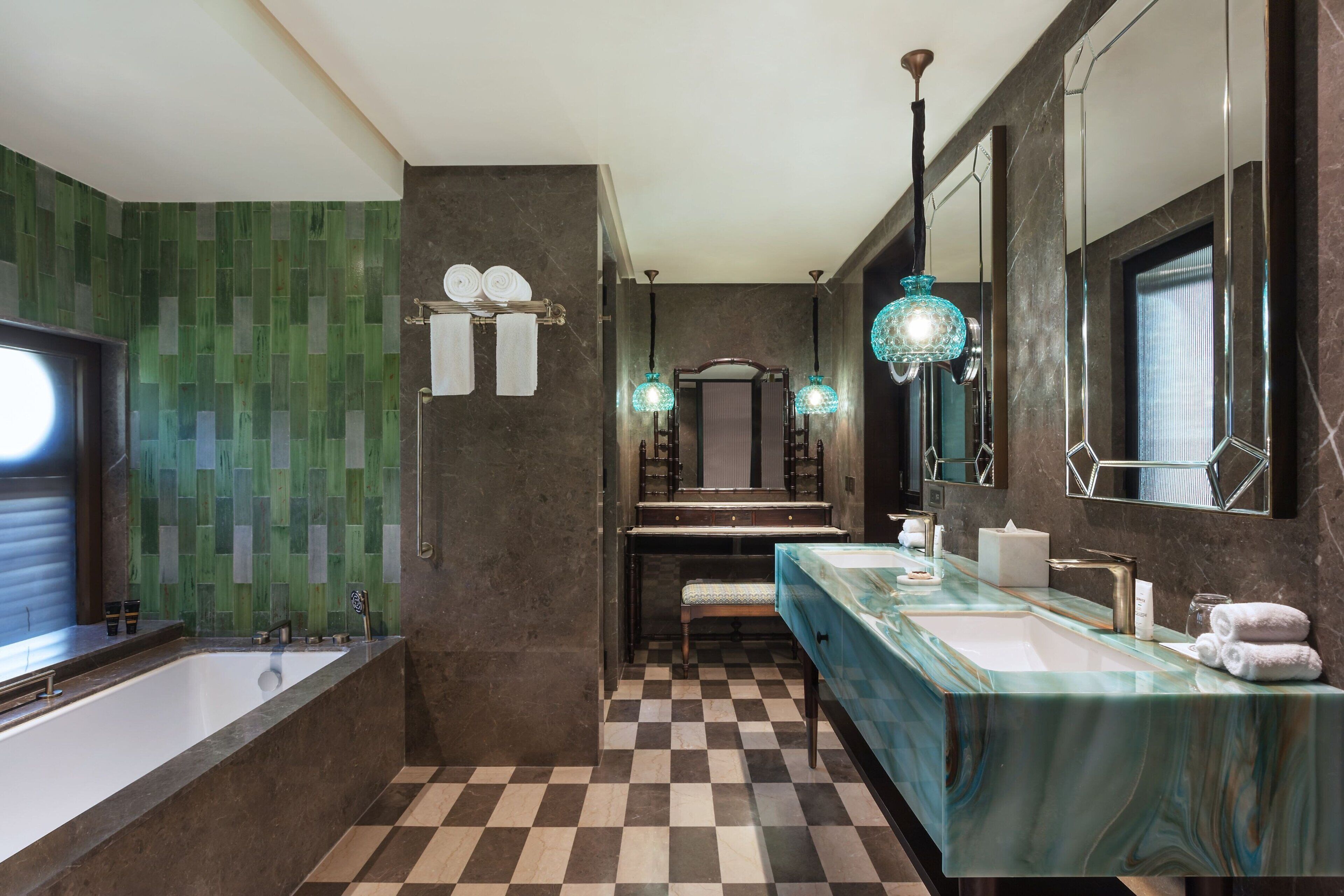 A modern bathroom with a checkered floor, a large bathtub, a vanity with a mirror, and a hanging light fixture.