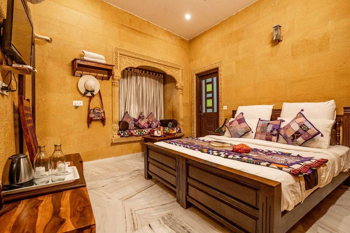 Une chambre à coucher avec un grand lit, une table de chevet en bois, un miroir, une fenêtre avec des rideaux et un luminaire fixé au mur.