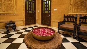 Un sol à carreaux, avec un bol décoratif rempli de pétales de roses placé au centre, flanqué de deux portes en bois ornées de motifs complexes et d’un banc doté d’une structure en bois foncé.
