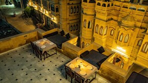 Un espace extérieur aménagé avec des tables et des chaises, entouré de murs en pierre et bordé d’un bâtiment doté de fenêtres en arc de cercle.