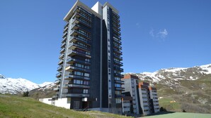 A modern high-rise building with multiple balconies, set against a backdrop of snow-capped mountains.