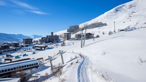 A snow-covered ski resort with modern buildings, ski lifts, and a clear blue sky.