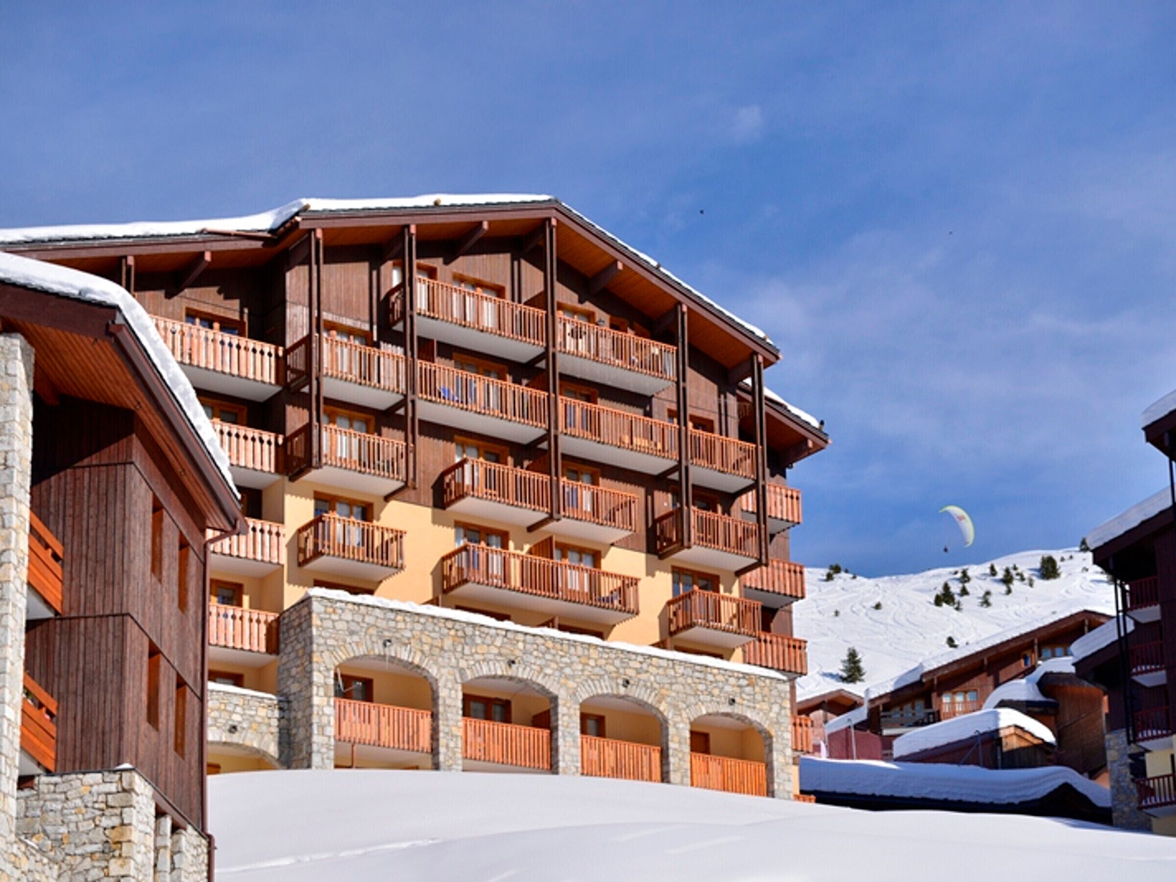 Ein mehrstöckiges Hotel mit Balkonen, Steinbögen und einer Skipiste im Hintergrund.