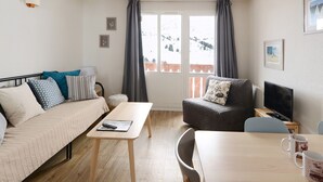 Een moderne, goed verlichte kamer met een bank, een kleintje tafeltje, een stoel en een televisie.