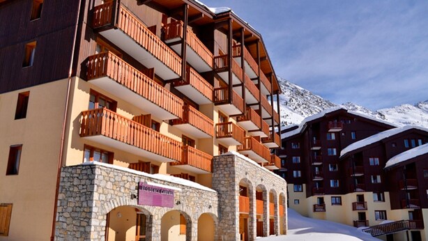 Een hotel met meerdere verdiepingen, houten balkons en stenen architectuur, gelegen voor een besneeuwde berg.