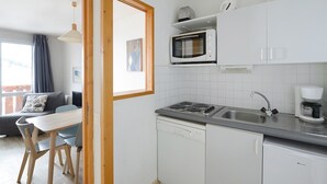 Een kleine keuken met witte kastjes, een magnetron, een koffiezetapparaat en een vaatwasser.