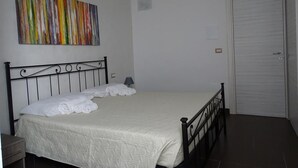 A bedroom with a bed, a nightstand, a wall-mounted painting, and a door. - Nonna Ia (Parabita)