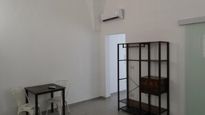 A room with a table and chairs, a black metal shelving unit, and an air conditioning unit on the wall. - Nonna Ia (Parabita)