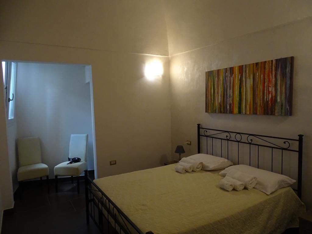 Camera da letto con un letto, due sedie, una lampada a parete e un quadro astratto dai colori vivaci.