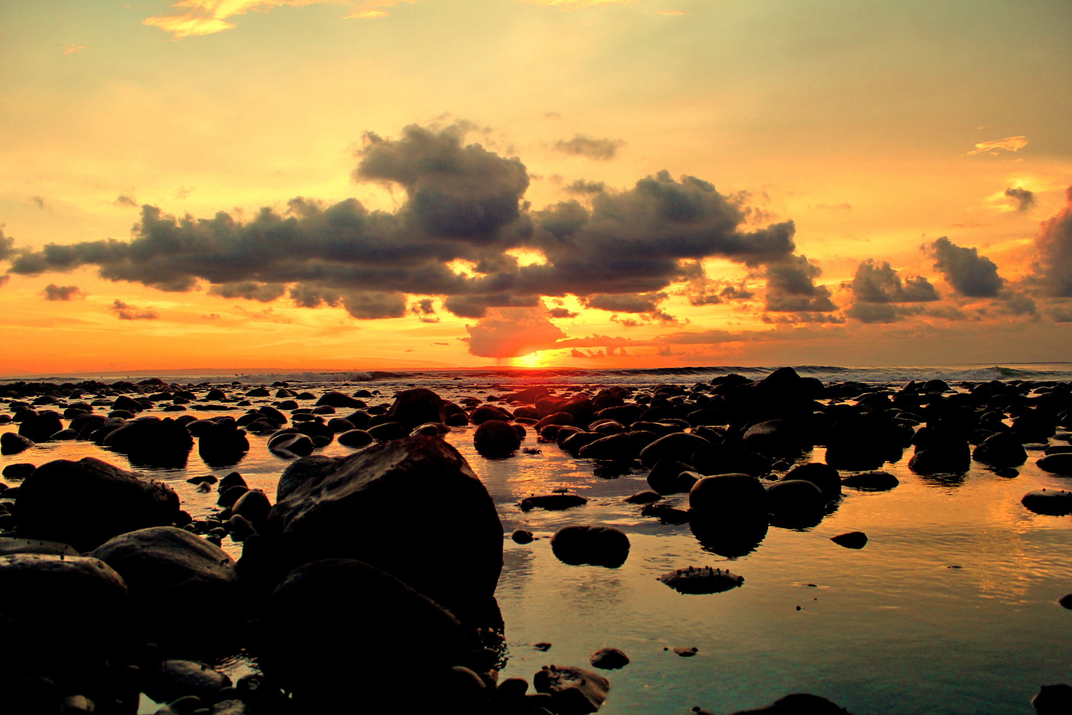 A rocky beach at sunset with the sun setting behind clouds.
