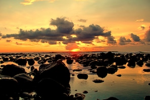 Una playa rocosa al atardecer, con el sol ocultándose tras las nubes.