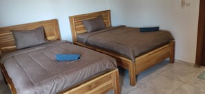 Dos camas de madera con ropa de cama y almohadas grises, una almohada azul en la cama de la izquierda y otra azul en la cama de la derecha.