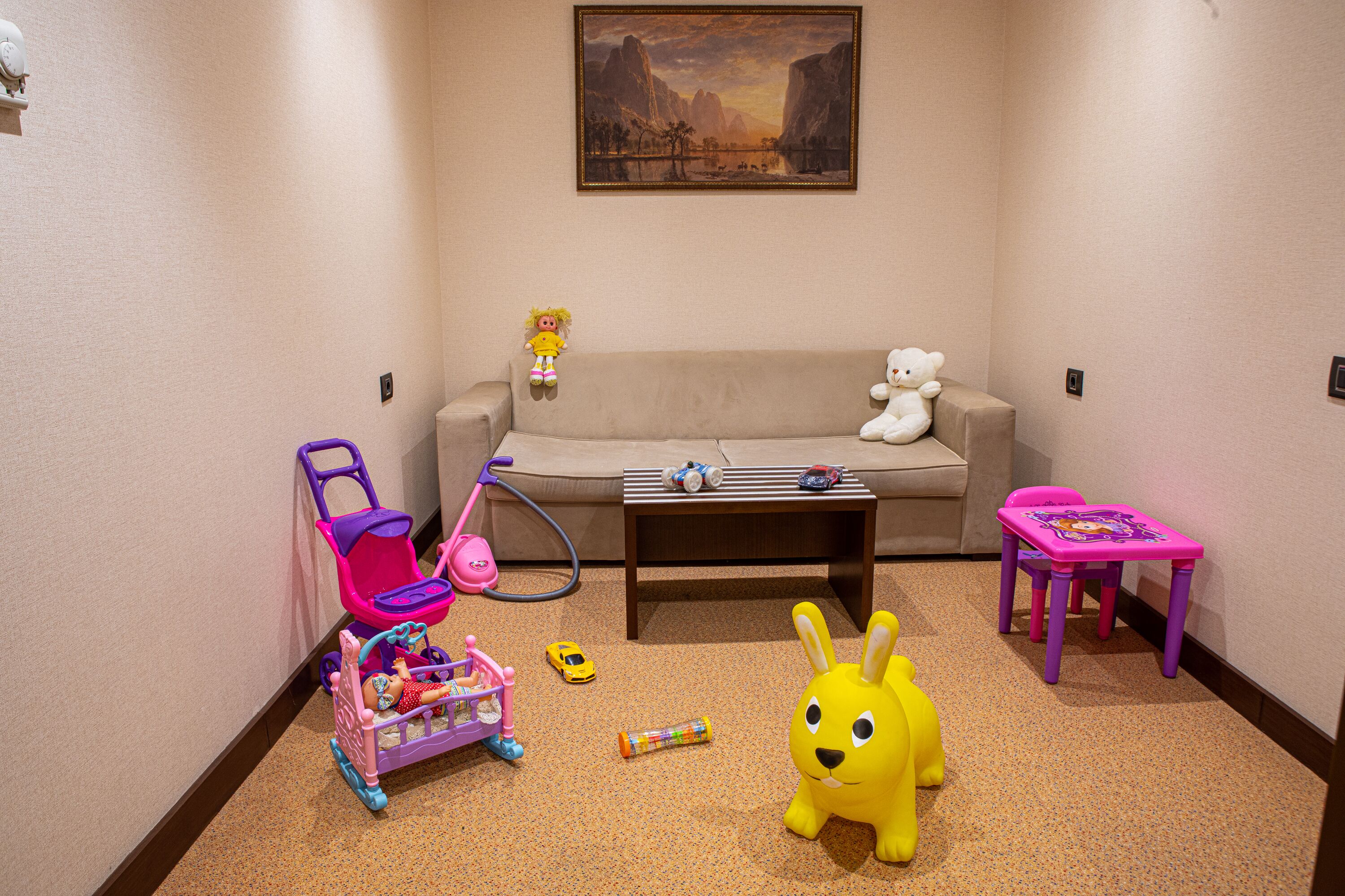 A child-friendly room with a sofa, a small table, a toy car, a toy bicycle, and a plush toy rabbit.