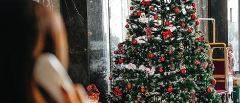 A Christmas tree decorated with ornaments and ribbons in a lobby area with marble walls and a reception desk.
