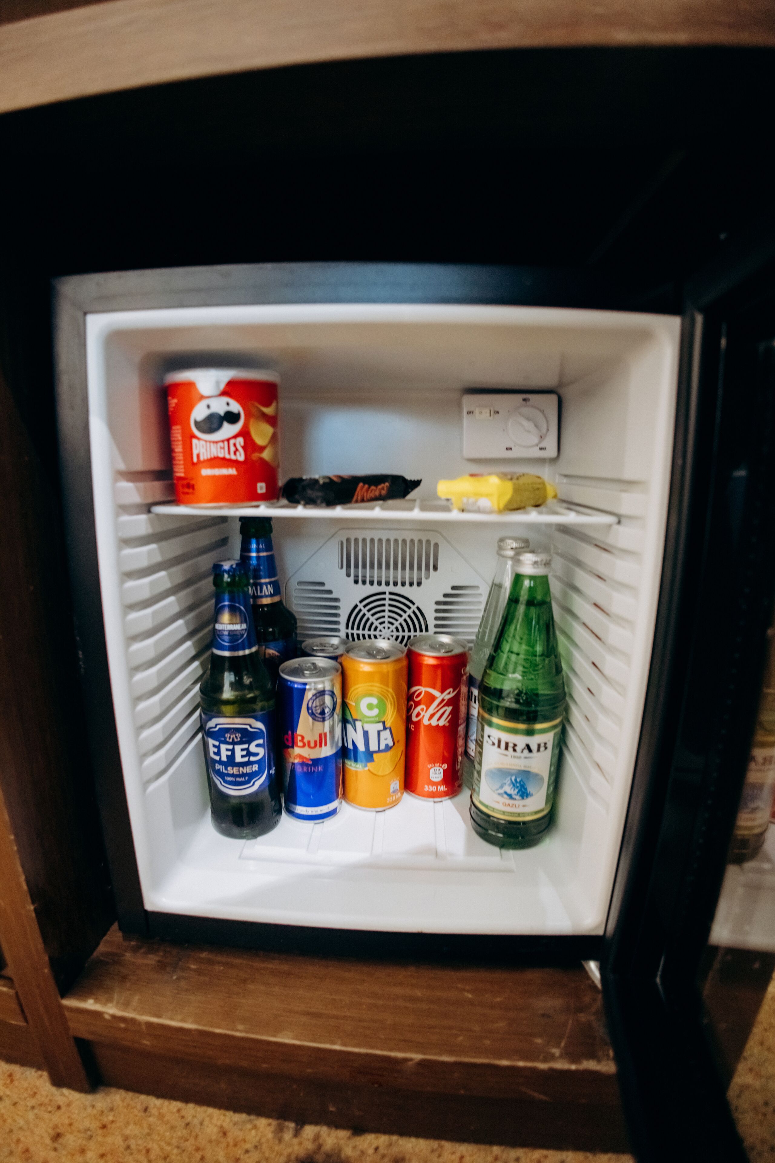 Ein gut sortierter Kühlschrank mit Getränken, darunter Pringles, Bier und Limonade.