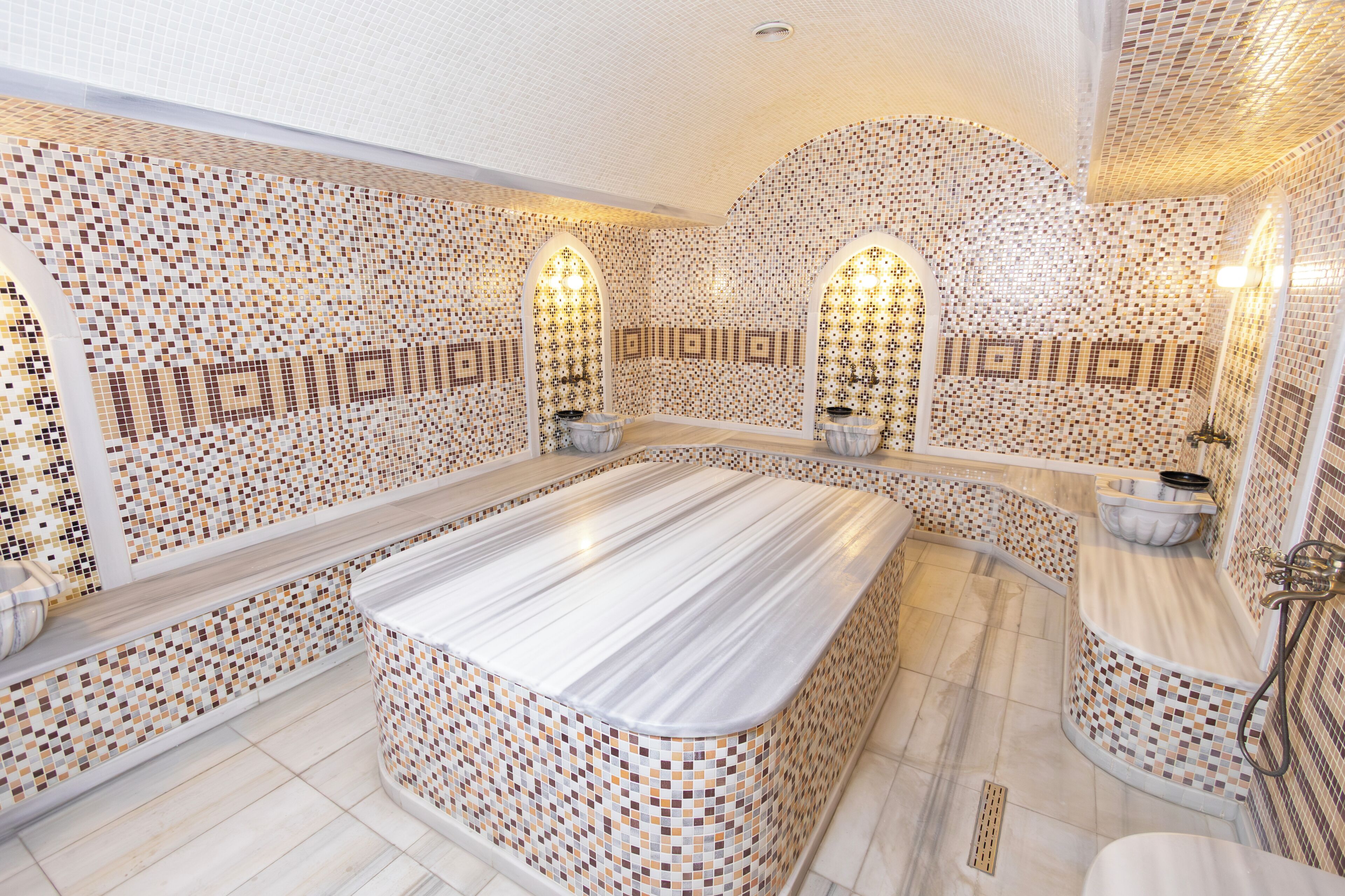 A spacious bathroom with a large marble sink, tiled walls, and a curved shower area.