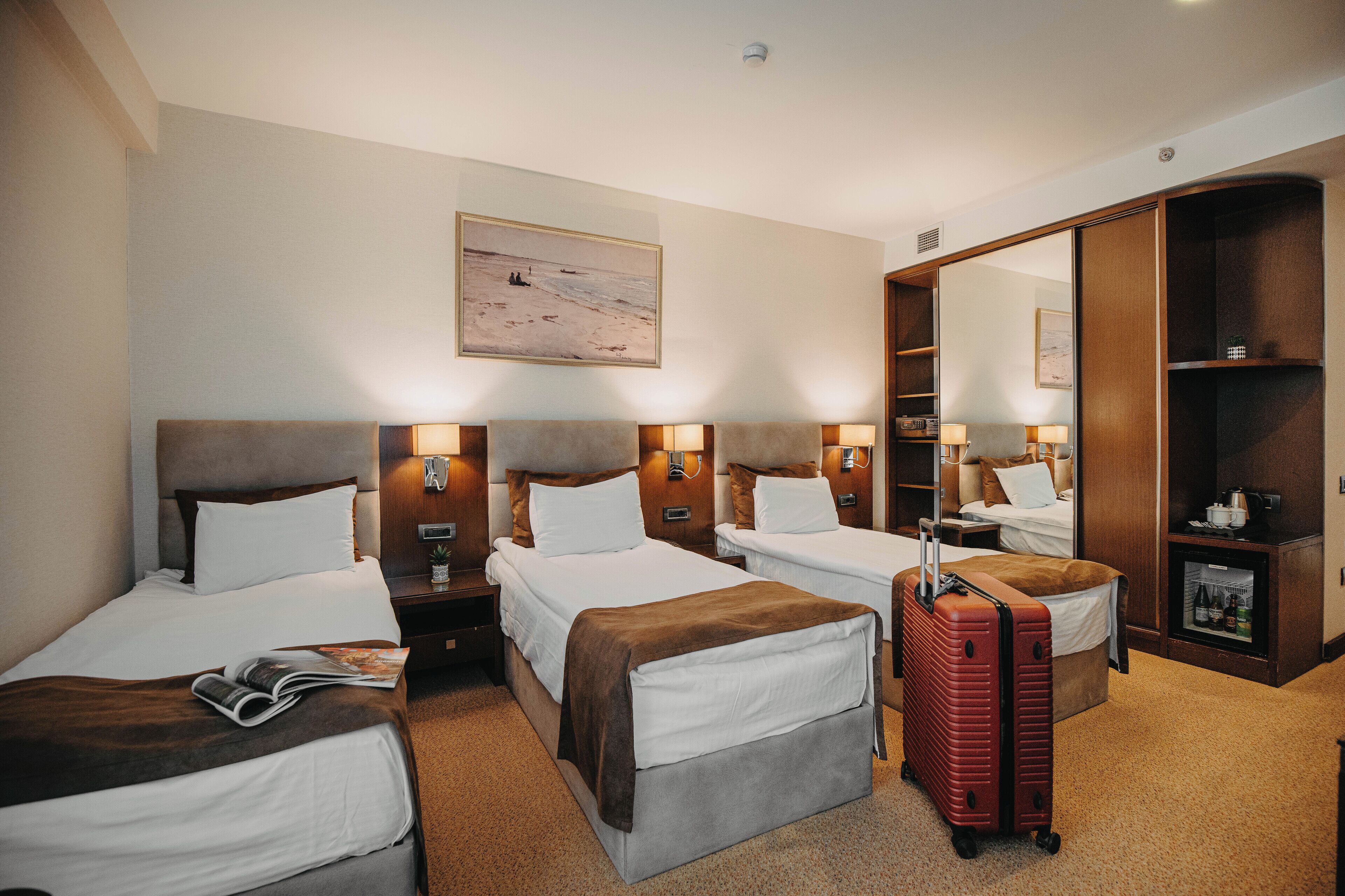 Habitación de hotel con dos camas, un espejo grande, un armario y una maleta.