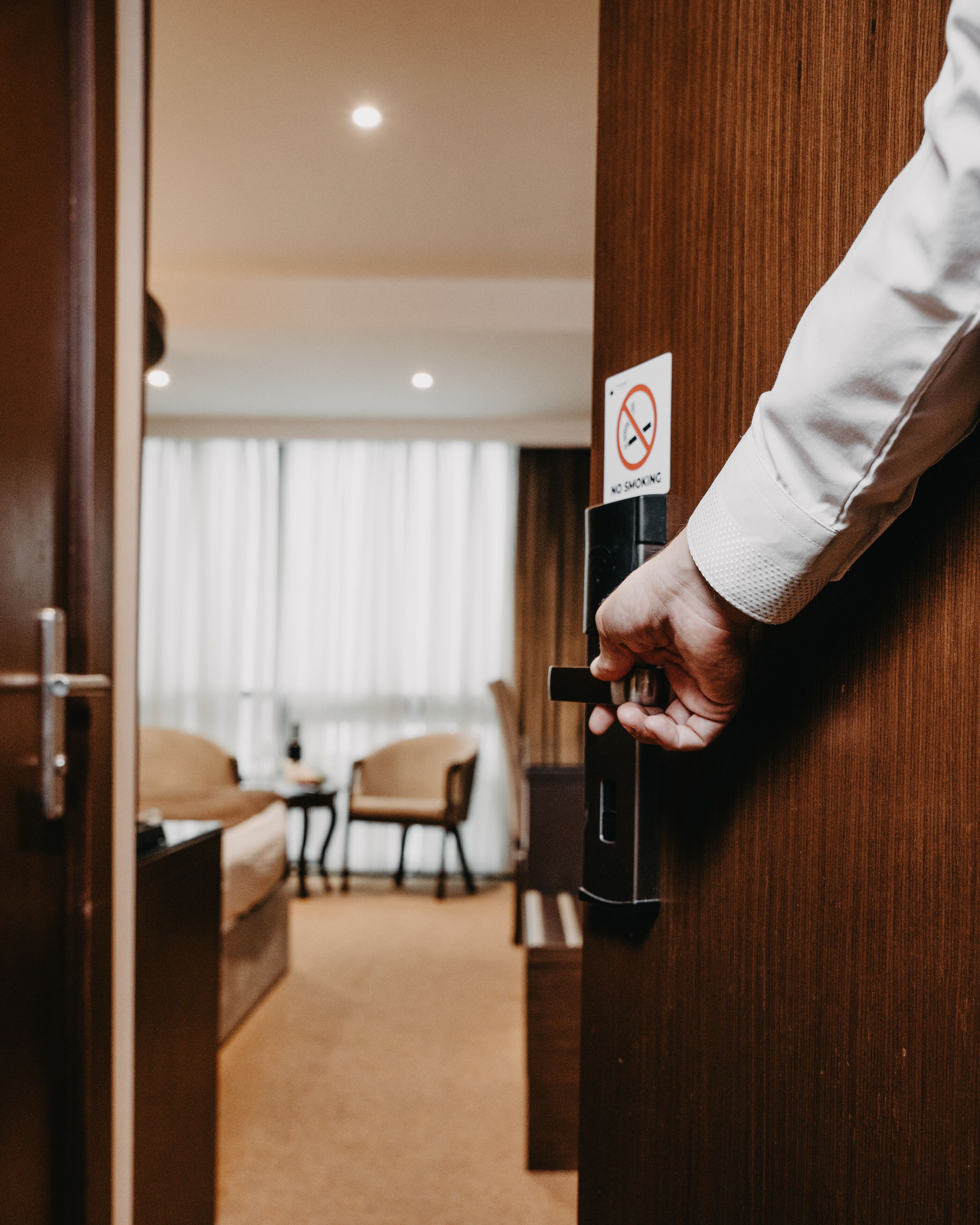 A hand opening a door to a hotel room with a no smoking sign on the door handle.