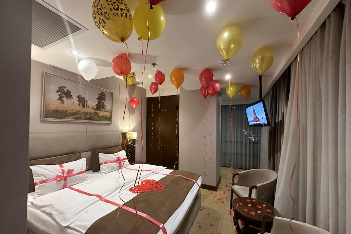 A hotel room with a bed, a TV, and balloons.