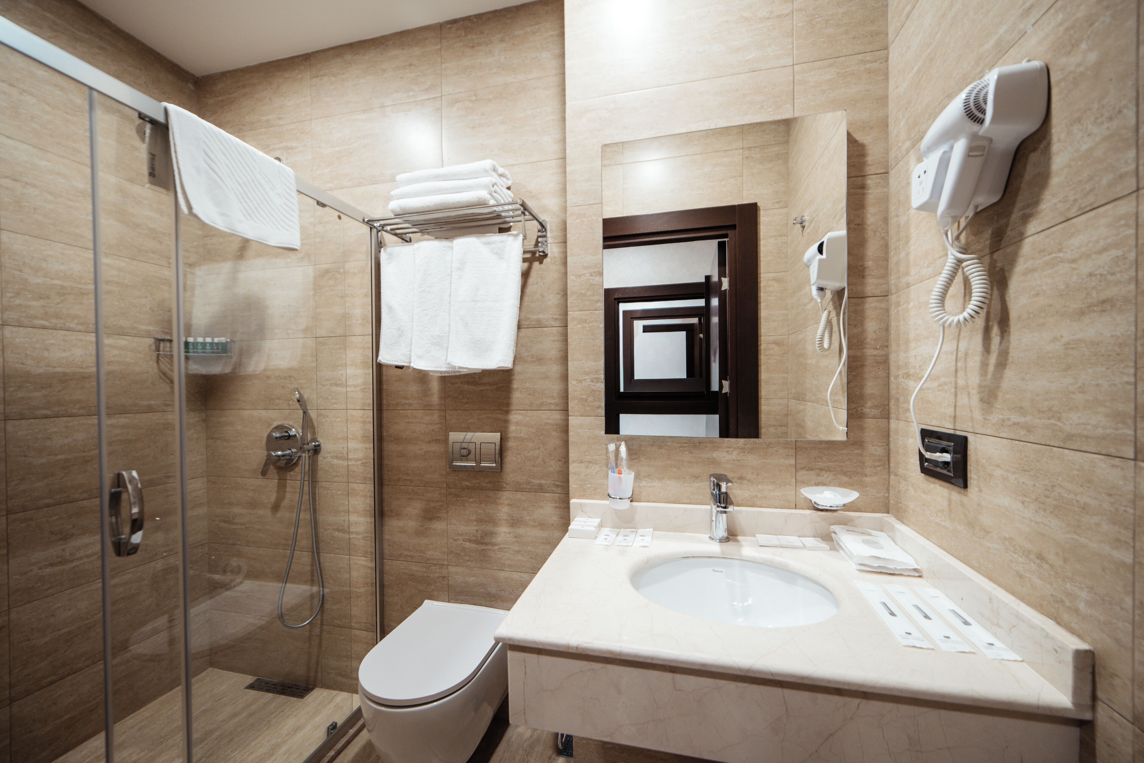 A modern bathroom with a glass shower enclosure, a toilet, a sink with a mirror above, and a hairdryer mounted on the wall.
