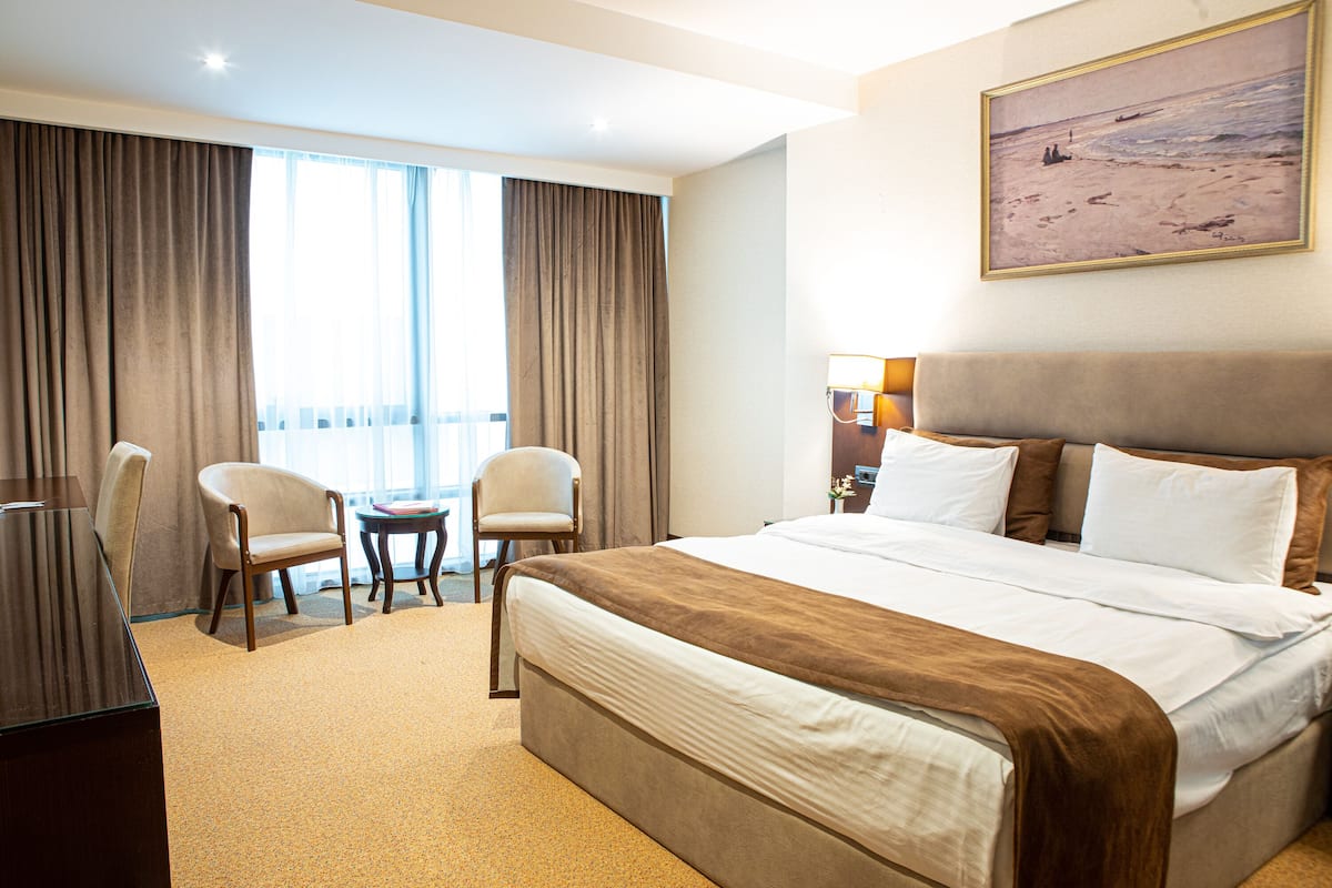 A hotel room with a large bed, two chairs, a desk, and a painting on the wall.