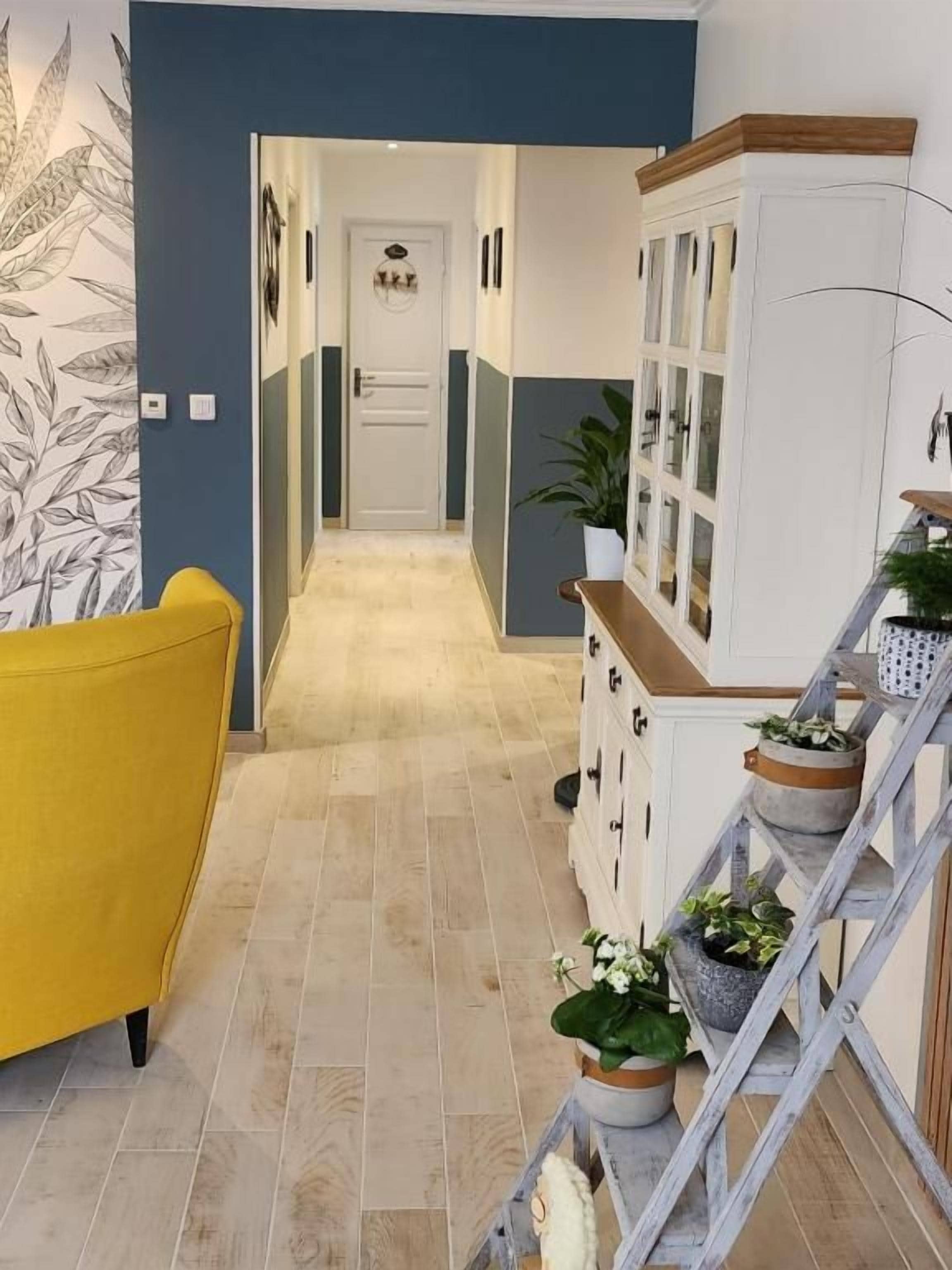 A hallway with a yellow chair, a staircase with potted plants, and a white cabinet.