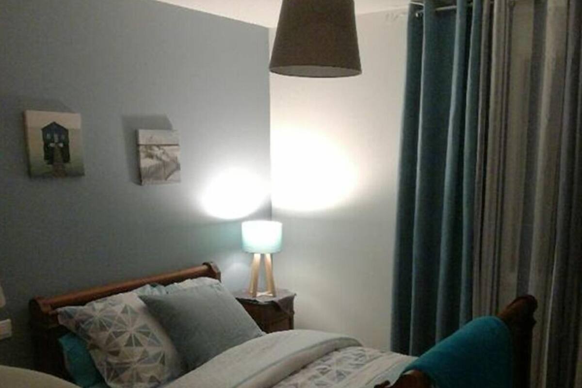 Un dormitorio con una cama, una lámpara de noche, un estante en la pared y una ventana con cortinas.