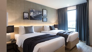 Een hotelkamer met twee bedden, een groot raam met gordijnen, een telefoon aan de muur en lijstwerken.