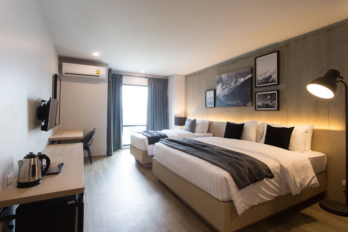 Une chambre d’hôtel moderne avec un grand lit, un bureau doté d’une bouilloire et un climatiseur fixé au mur.
