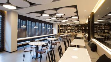 A modern library with round tables, bookshelves, and a large window with blinds.