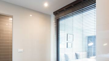 A modern bathroom with a large bathtub, a window with blinds, and a shower area.