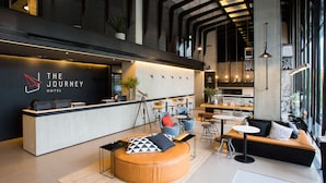 Een moderne hotellobby met een receptiebalie, zithoeken en een groot raam dat voor natuurlijk licht zorgt.