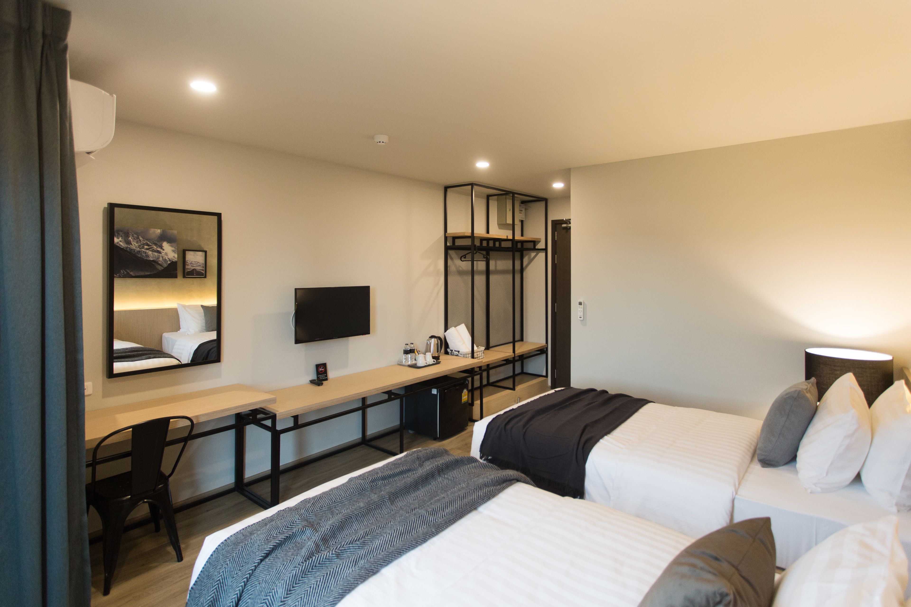 A hotel room with two beds, a desk, a chair, a TV, and a mirror.