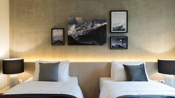 A hotel room with two beds, a large wall-mounted picture of mountains, and a neutral color scheme.