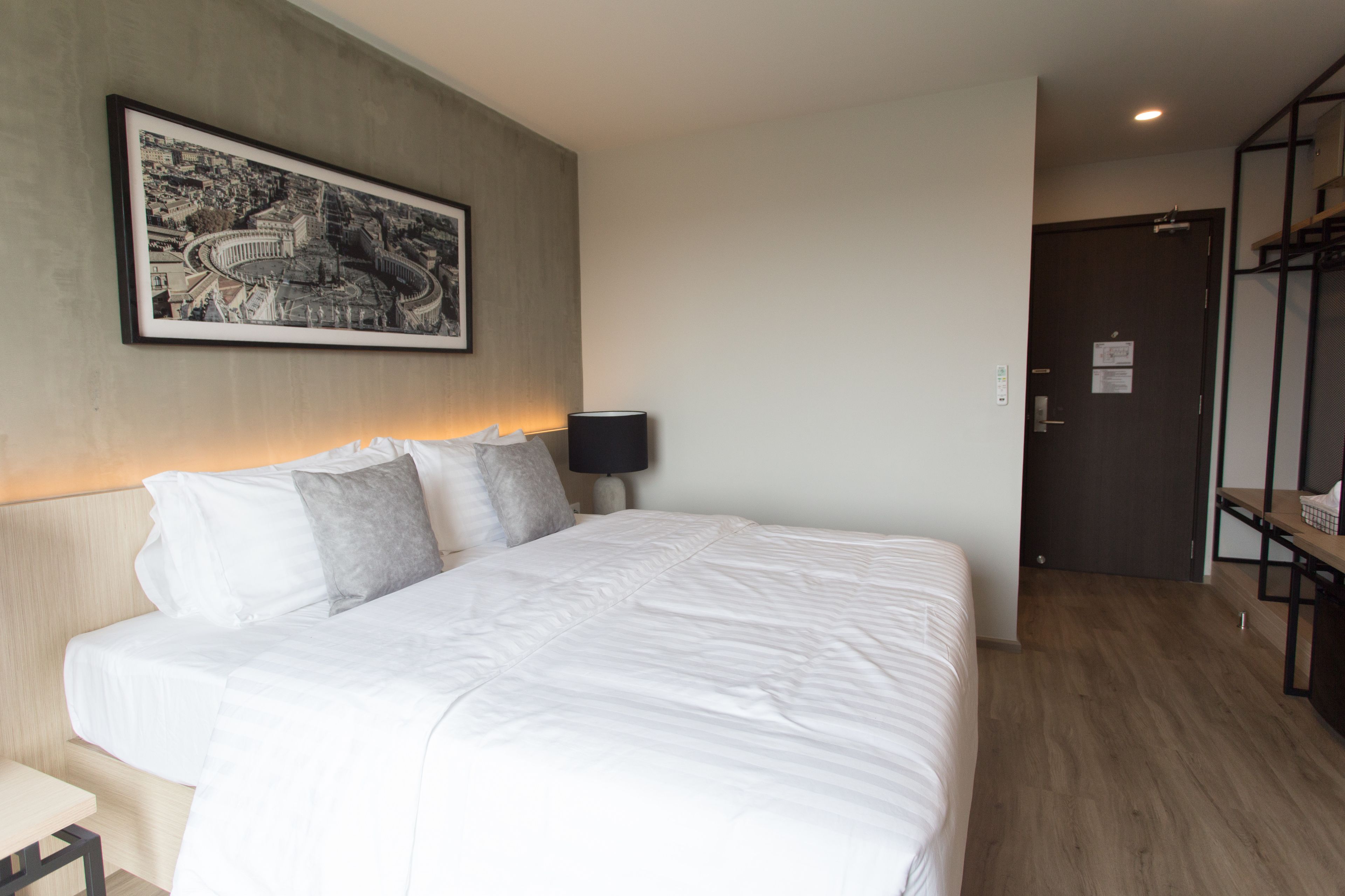 A hotel room with a large bed, a framed cityscape picture, a bedside lamp, and a wooden floor.