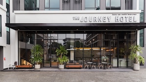 Hotel The Journey, met een moderne gevel, grote glasramen en een buiten zitgedeelte met plantenpotten.