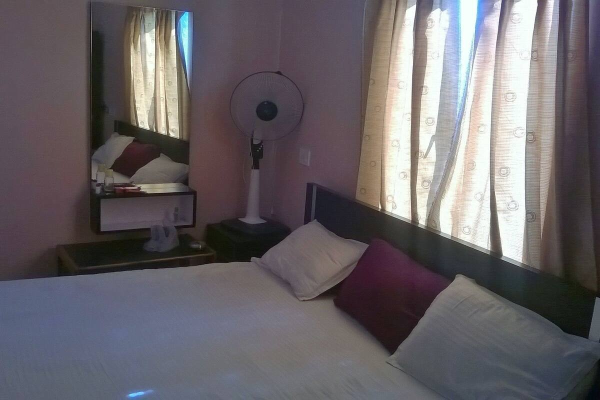 Quarto de hotel com cama, mesa de cabeceira, espelho, ventoinha e cortinas.