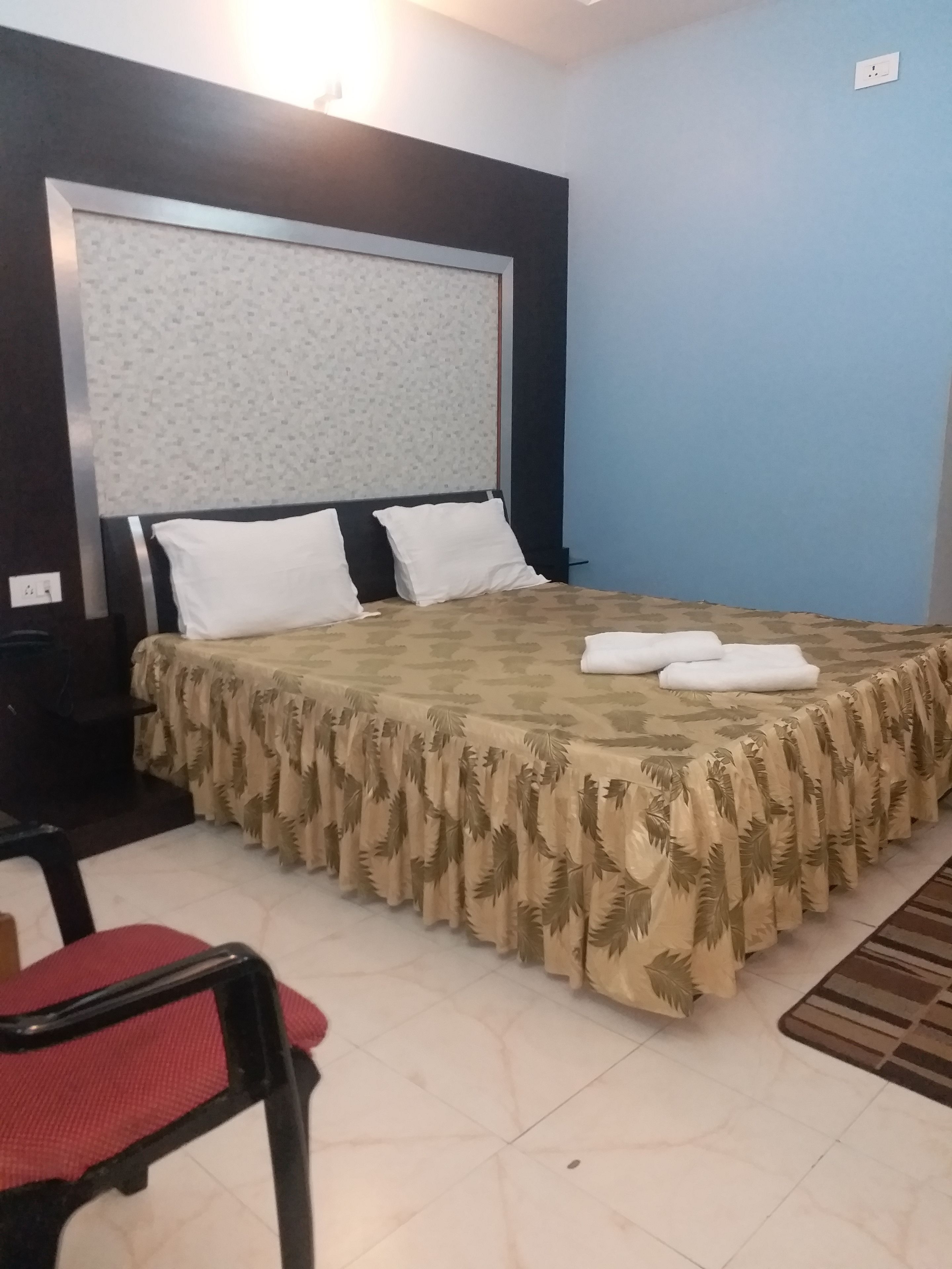 Una cama bien hecha con un edredón estampado y almohadas, una silla con un cojín rojo y una alfombra pequeña en el suelo.