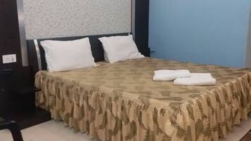 Una cama bien hecha con un edredón estampado y almohadas, una silla con un cojín rojo y una alfombra pequeña en el suelo.