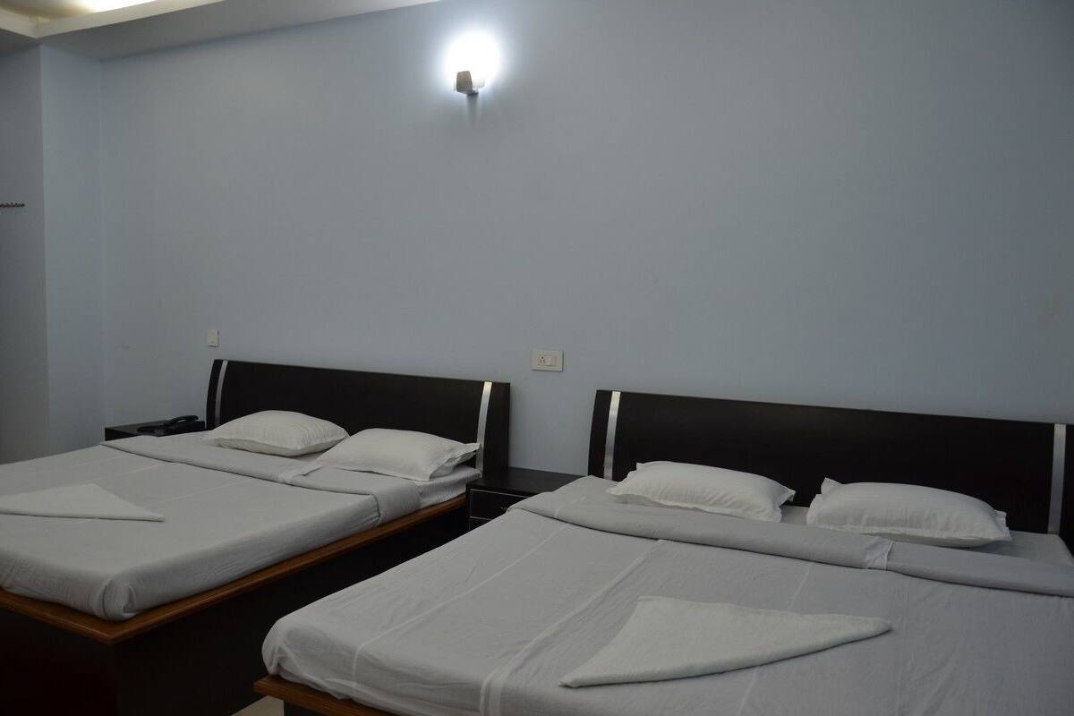 Quarto com duas camas de solteiro, cada uma com roupa de cama branca e cabeceira de madeira. Há um luminário fixado na parede sobre as camas.