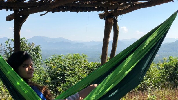 A person relaxing in a hammock under a wooden pergola with a mountainous landscape in the background.