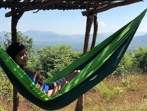 A person relaxing in a hammock under a wooden pergola with a mountainous landscape in the background. - Canary Forest Camping (Paud)
