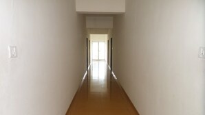 En lång, smal hall med vita väggar och ett trägolv, som leder in till ett ljust rum med ett stort fönster.