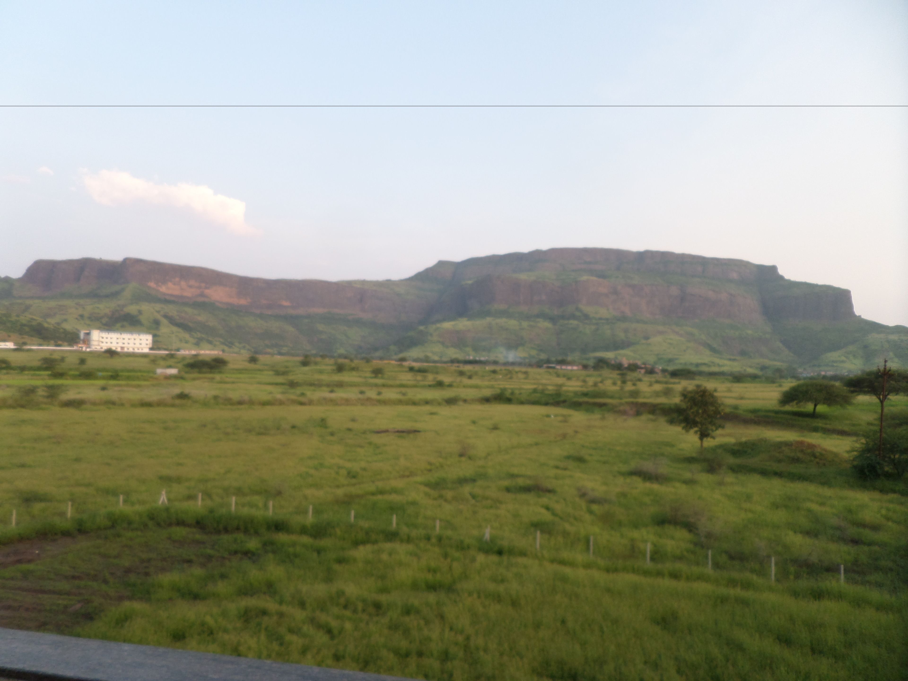 A large building with multiple floors, surrounded by a green field and a hill in the background.