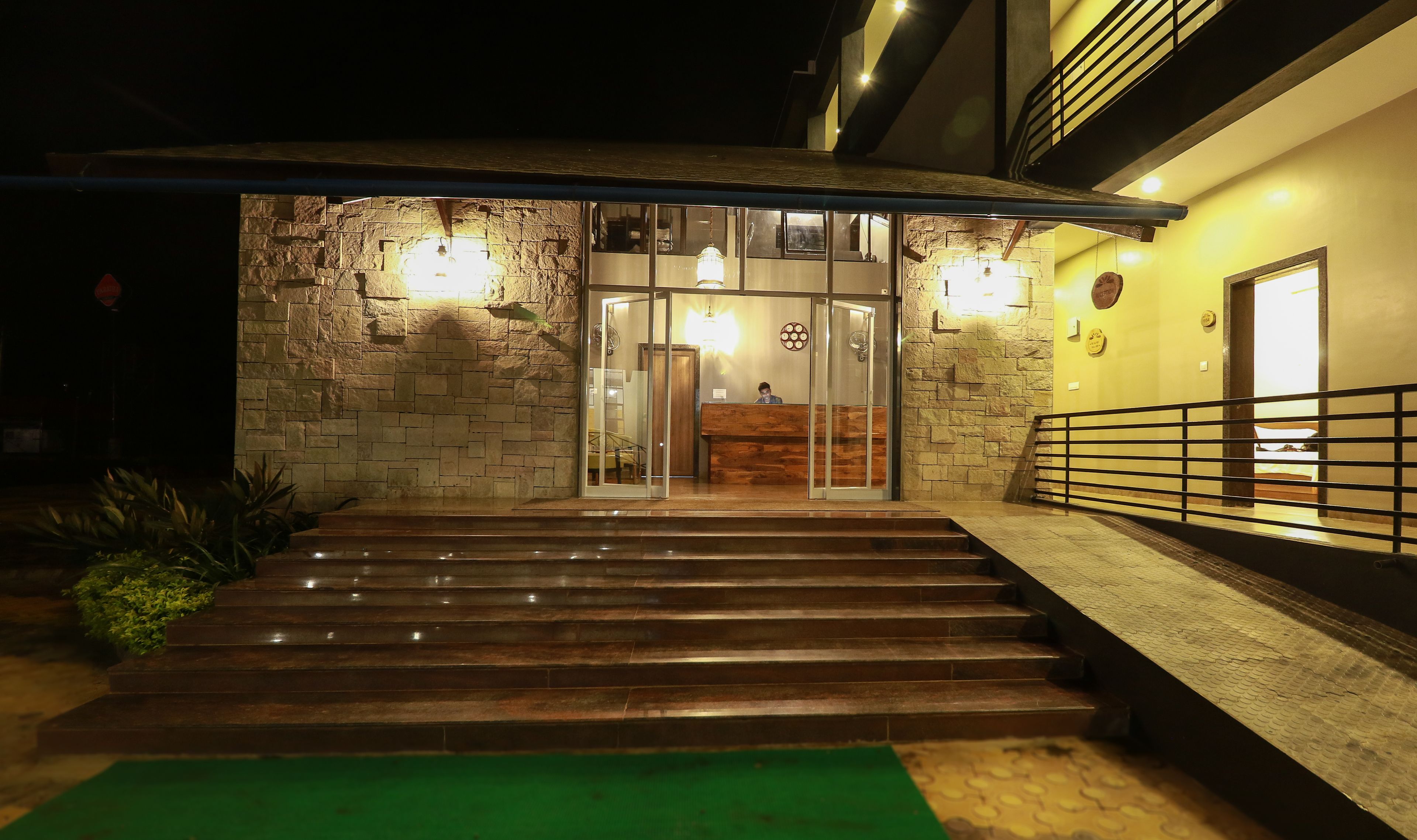A hotel entrance with stone walls, a reception desk, and a staircase leading to the entrance.