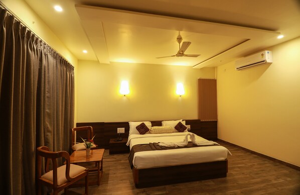 A hotel room with a bed, a desk, a chair, a ceiling fan, and wall-mounted lights.