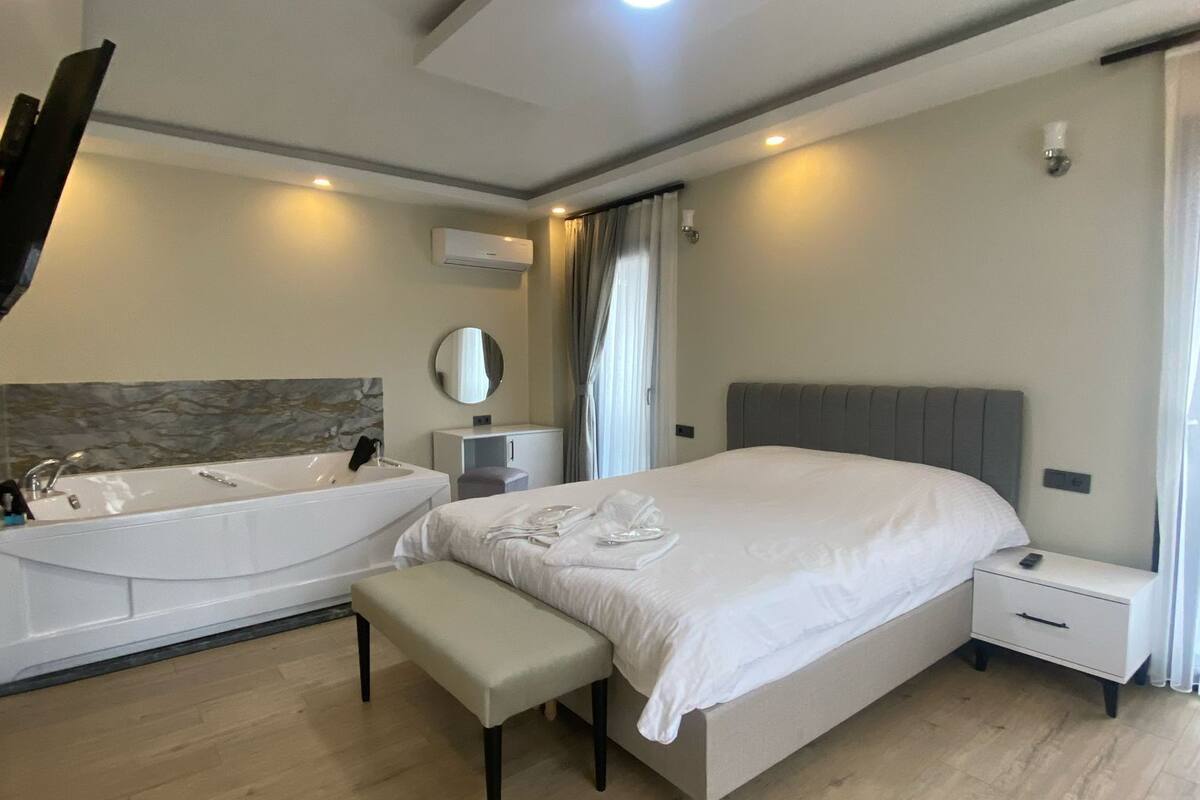 Ein modernes Hotelzimmer mit einem großen Bett, einem eigenen Badezimmer mit einer Badewanne, einem Nachttisch und einer Bank.