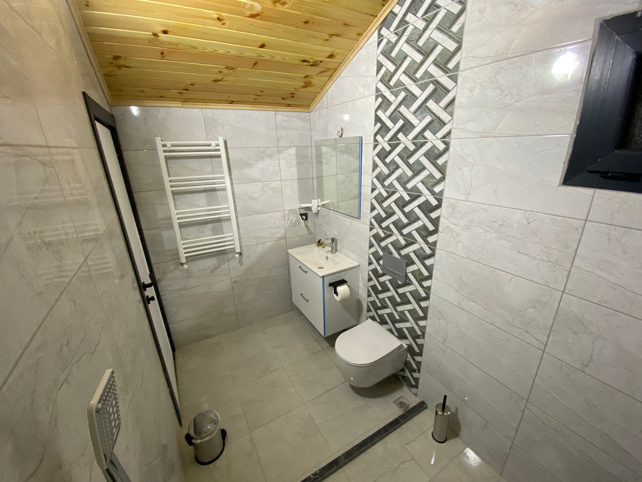 Een moderne badkamer met een houten plafond, een witte wastafel, een toilet en een behang met patroon.