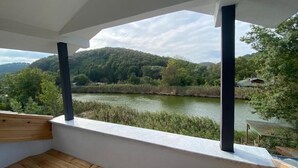 A balcony with a view of a river and forested hills.